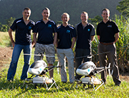 Five men stand behind two UAV helicopters