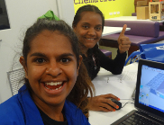 Two female students show thumbs up with a laptop computer on the desk.