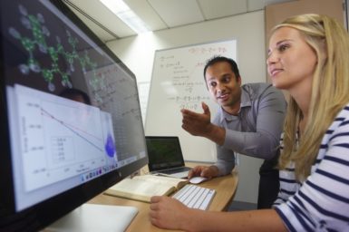 Male and female researchers examine data on computer screen.