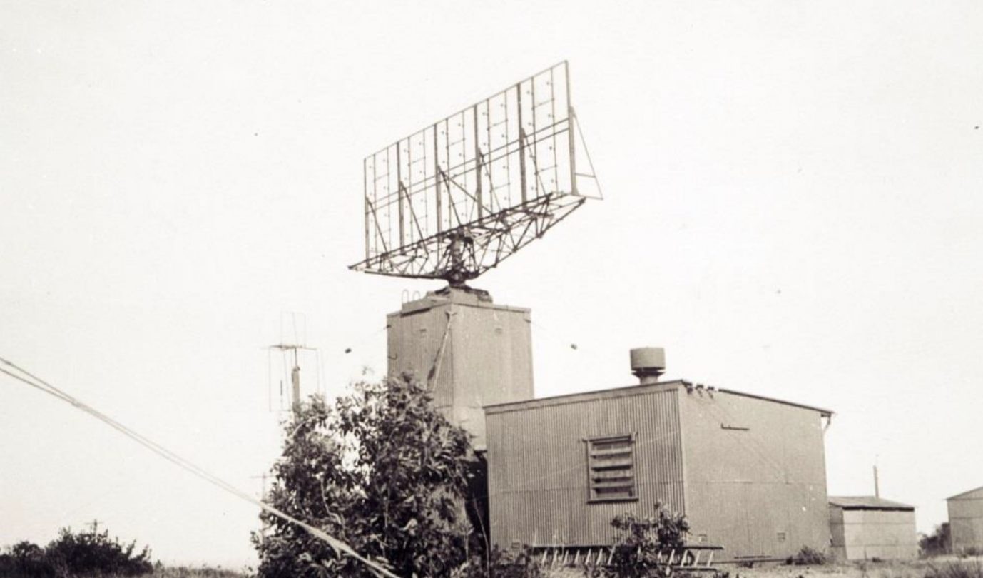 Black and white image of a building with a large antenna on the roof