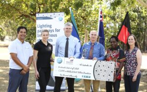 Six people standing in a treed garden, holding an oversized cheque in front of flags and CSIRO information panel poster.