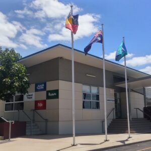 Outside facade of one of the Glenala State High School buildings with three flag poles in front. 