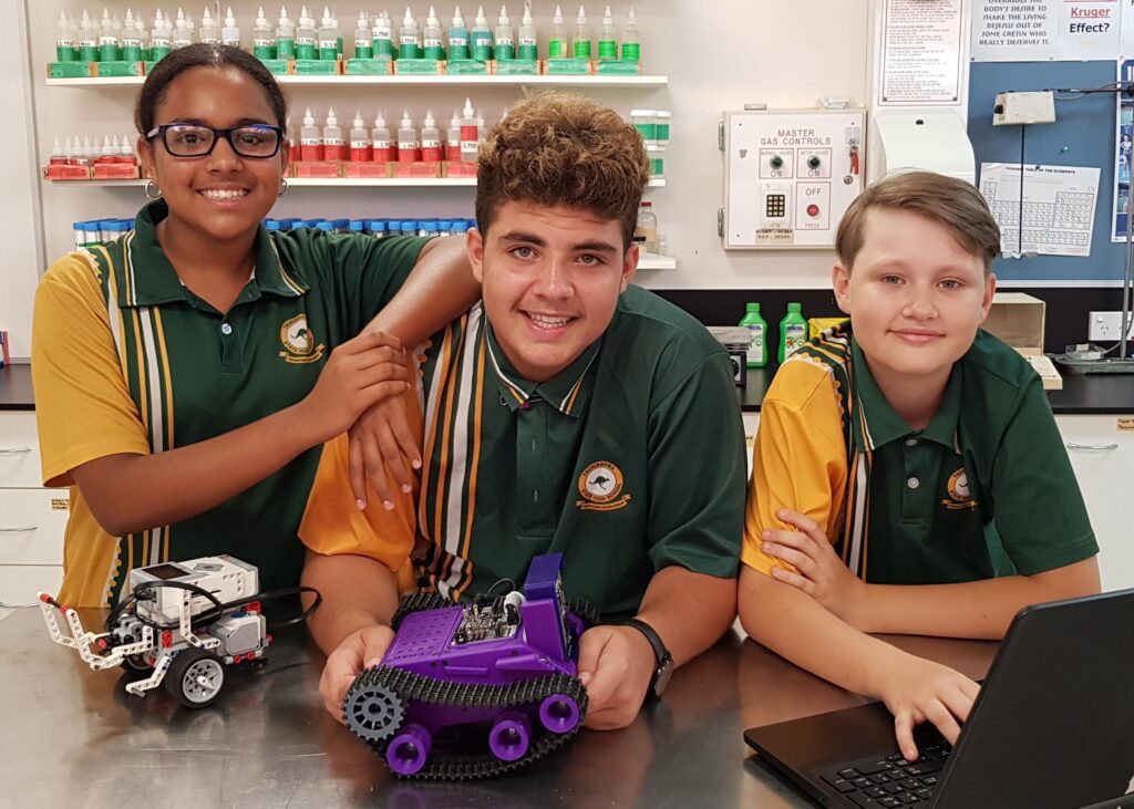 Three Thuringowa State High School student standing in lab with a laptop and robots in front of them.