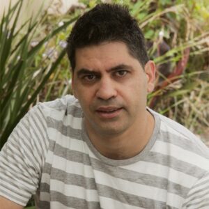 Head and shoulders photo of Tuguy Esgin in front of garden vegetation. 